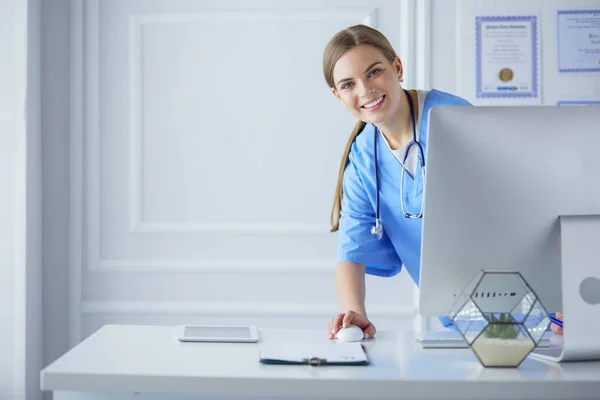 Portrait of female physician using laptop computer while standing near reception desk at clinic or emergency hospital