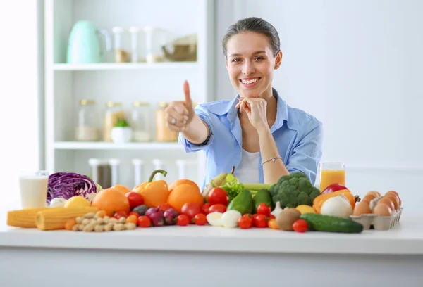 Junge und süße Frau sitzt am Tisch voller Obst und Gemüse im hölzernen Innenraum. — Stockfoto