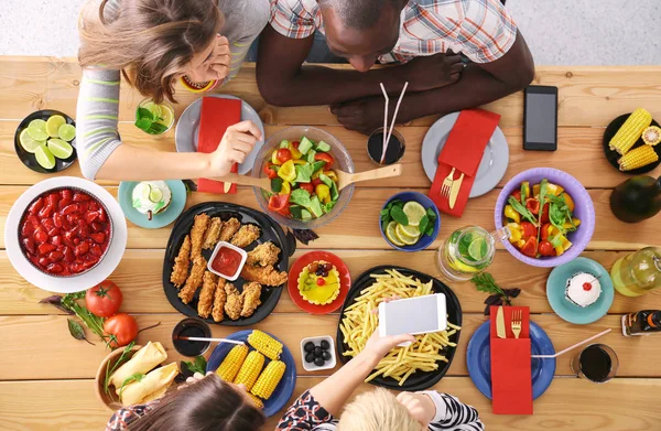 Vue du dessus du groupe de personnes qui dînent ensemble tout en étant assis à une table en bois. De la nourriture sur la table. Les gens mangent fast food. — Photo