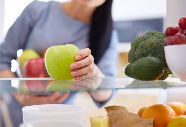 Gülümseyen kadın buzdolabından taze meyve alıyor, sağlıklı yiyecek konsepti.