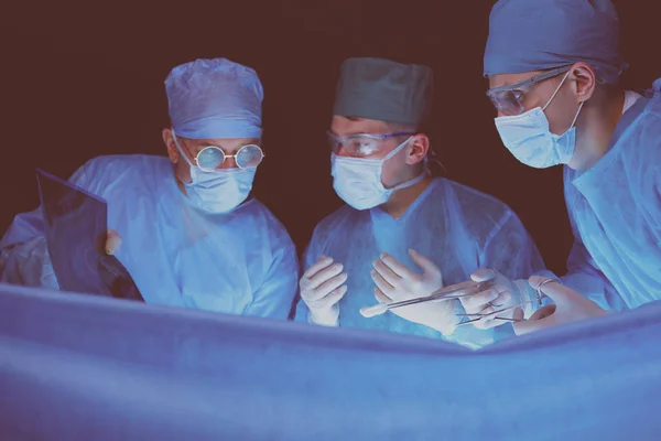 Grupo de cirujanos trabajando en quirófano tonificado en azul. Equipo médico realizando la operación — Foto de Stock