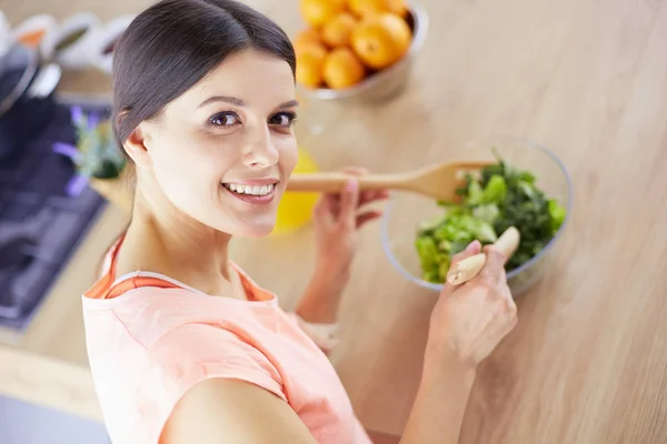 Mujer joven sonriente mezclando ensalada fresca en la cocina. —  Fotos de Stock