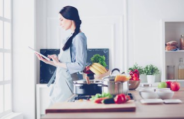 Mutfakta yemek yapmak için tablet bilgisayar kullanan genç bir kadın.