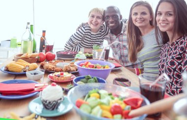 Ahşap masada otururken birlikte yemek yiyen bir grup insanın üst düzey görüntüsü. Masada yemek var. İnsanlar fast food yiyor..