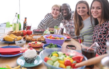 Ahşap masada otururken birlikte yemek yiyen bir grup insanın üst düzey görüntüsü. Masada yemek var. İnsanlar fast food yiyor..