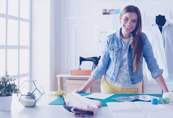 Schöne Modedesignerin steht neben Schreibtisch im Atelier — Stockfoto