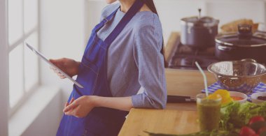 Mutfakta yemek yapmak için tablet bilgisayar kullanan genç bir kadın.