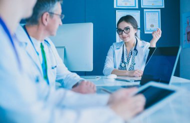 Ciddi bir tıbbi ekip parlak bir ofiste dizüstü bilgisayar kullanıyor.