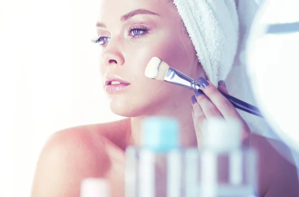 Et billede af en ung kvinde, der anvender ansigtspulver i badeværelset - Stock-foto
