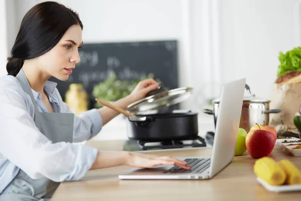 Young Woman in kitchen with laptop computer looking recipes, smiling. Food blogger concept — Stock Photo, Image