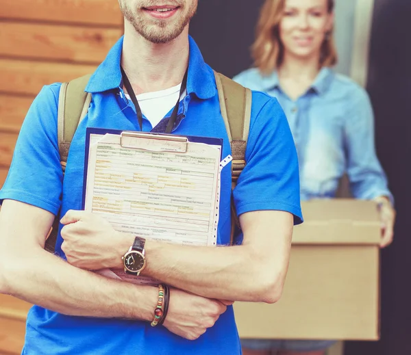 Repartidor sonriente con uniforme azul que entrega la caja de paquetes al destinatario: concepto de servicio de mensajería. Repartidor sonriente en uniforme azul —  Fotos de Stock