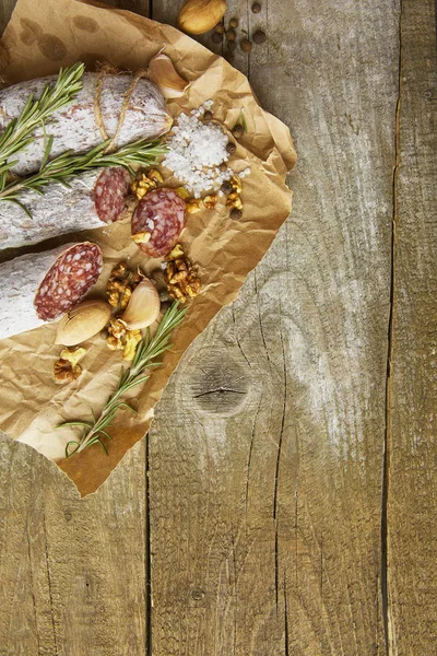 Italian salami wih sea salt, rosemary, garlic and nuts on paper. Rustic style. Top view. — Stock Photo, Image