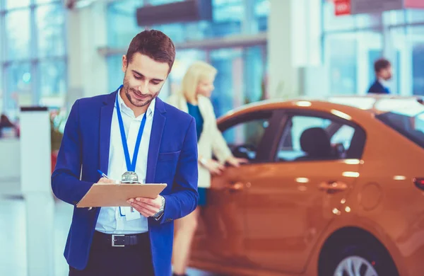 Distribuidor de mujer se para cerca de un coche nuevo en la sala de exposición — Foto de Stock