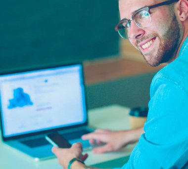 Genç adam kullanarak telefon ve dizüstü bilgisayarda çalışır