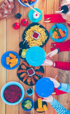 Ahşap masada otururken birlikte yemek yiyen bir grup insanın üst düzey görüntüsü. Masada yemek var. İnsanlar fast food yiyor..