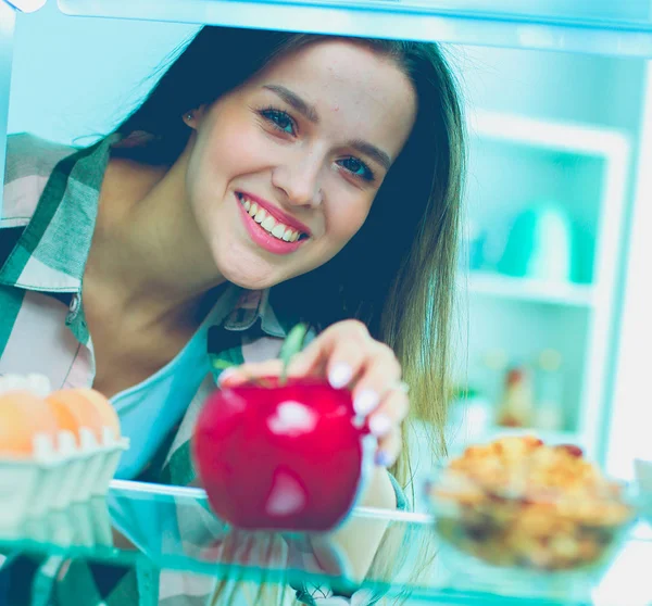 Портрет жінки, що стоїть біля відкритого холодильника, повний здорової їжі, овочів і фруктів — стокове фото
