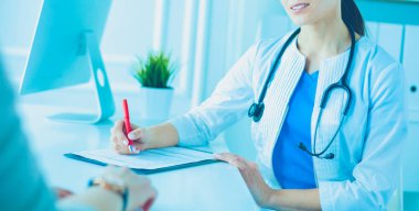 Doktor ve hasta hastane danışma odasında tıbbi sorunları tartışıyorlar. Doktor hasta formunu dolduruyor.