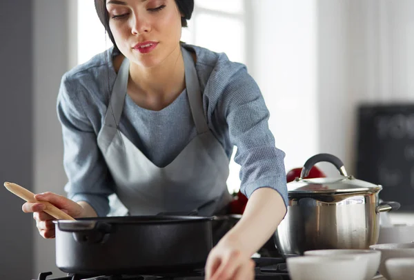 Mujer parada junto a la estufa en la cocina, cocinando y oliendo los agradables aromas  . — Foto de Stock