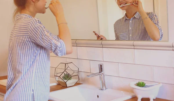 Jovem mulher bonita escovando os dentes na frente do espelho — Fotografia de Stock
