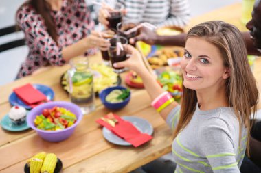 Ahşap masada otururken birlikte yemek yiyen bir grup insanın üst düzey görüntüsü. Masada yemek var. İnsanlar fast food yiyor. Bir kızın portresi.