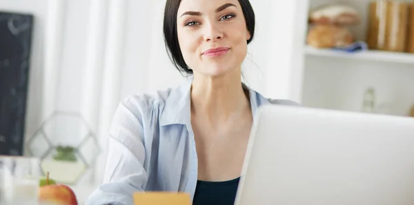 Χαμογελαστή γυναίκα online ψώνια χρησιμοποιώντας υπολογιστή και πιστωτική κάρτα στην κουζίνα — Φωτογραφία Αρχείου