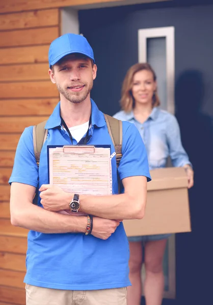 Smiling delivery man in blue uniform delivering parcel box to recipient - courier service concept. Smiling delivery man in blue uniform