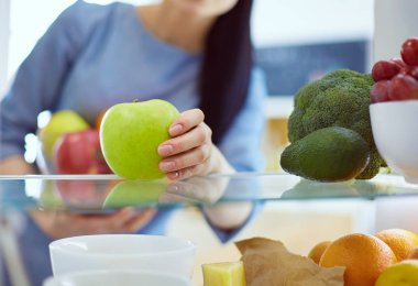 Gülümseyen kadın buzdolabından taze meyve alıyor, sağlıklı yiyecek konsepti.