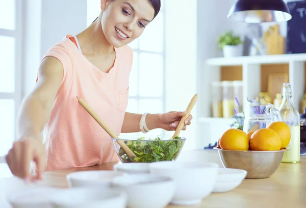 Leende ung kvinna blandar färsk sallad i köket. — Stockfoto