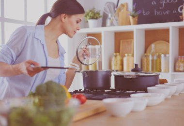 Mutfakta sobanın yanında duran genç bir kadın.