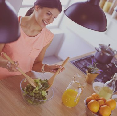 Gülümseyen genç kadın mutfakta taze salata karıştırıyor..
