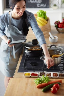 Tablette tarifi takip eden bir kadın evde yemek pişiriyor.