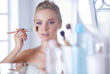 Genç bir kadının banyoya yüz pudrası sürerken fotoğrafı.