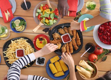 Ahşap masada otururken birlikte yemek yiyen bir grup insanın üst düzey görüntüsü. Masada yemek var. İnsanlar fast food yiyor..