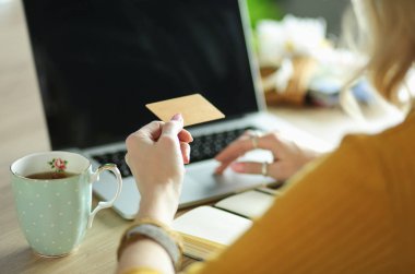 Kredi kartı tutan ve dizüstü bilgisayar kullanan genç bir kadın. Çevrimiçi alışveriş kavramı