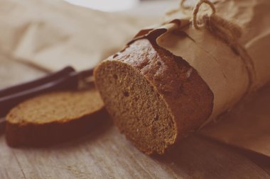 Tahta masanın üzerinde kağıda sarılı bir somun ekmek.