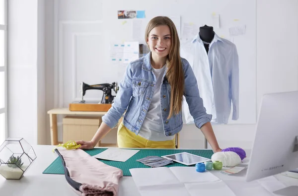 Mooie mode-ontwerper staat in de buurt van bureau in studio — Stockfoto