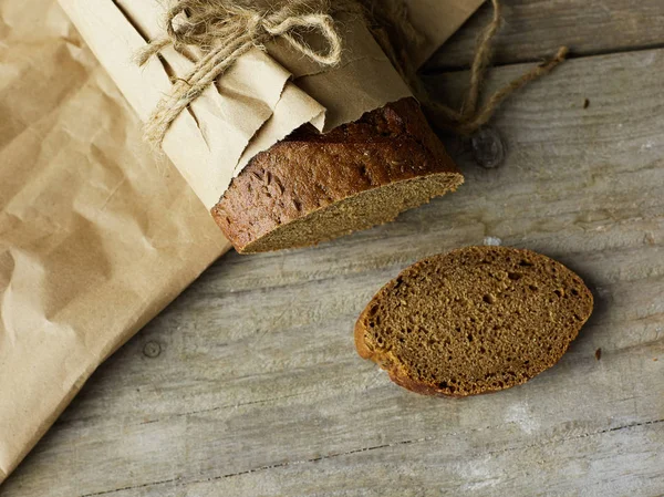 Krájený bochník chleba zabalený v papíru na dřevěném stole — Stock fotografie