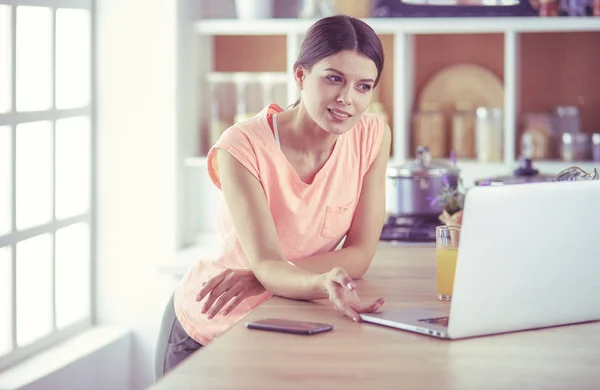 Mooie vrouw aan de telefoon met behulp van laptop thuis in de keuken — Stockfoto