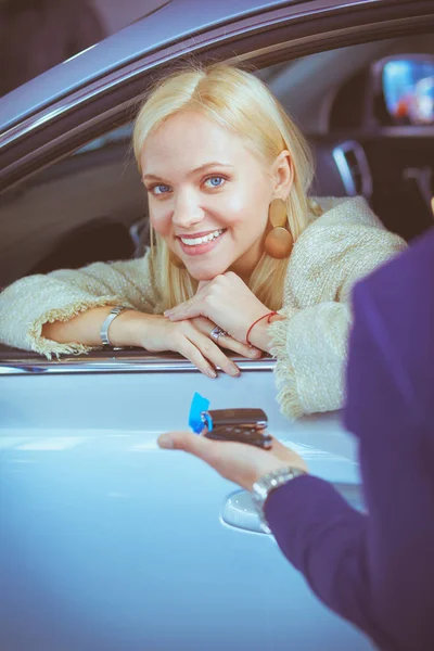 Vendedor de coches vende un coche a cliente feliz en concesionario de coches y las manos sobre las llaves . — Foto de Stock
