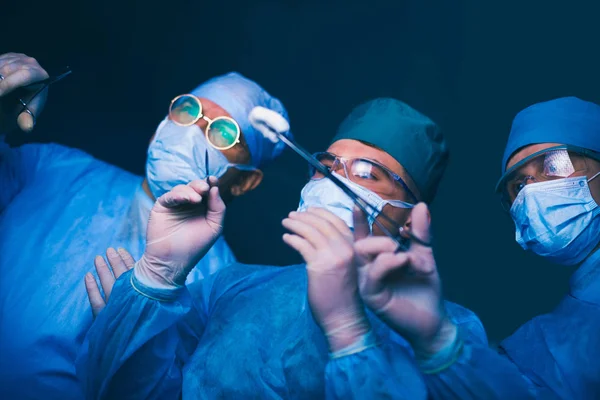 Grupo de cirurgiões no trabalho em sala de operações tonificada em azul. Equipe médica realizando operação — Fotografia de Stock