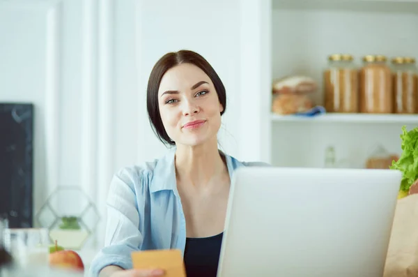 Smiling woman online shopping using computer and credit card in kitchen — Stock Photo, Image