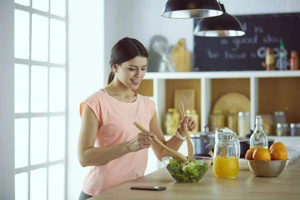 Mujer joven sonriente mezclando ensalada fresca en la cocina. — Foto de Stock