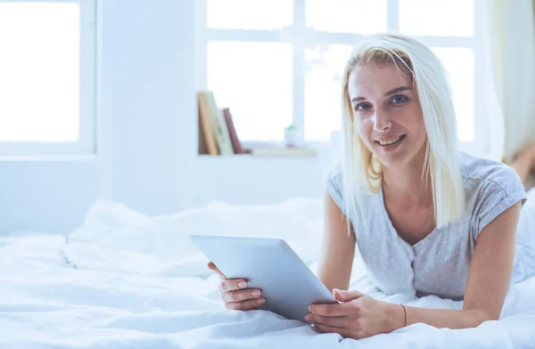 Menina segurando tablet digital com tela em branco e sorrindo para a câmera no quarto — Fotografia de Stock