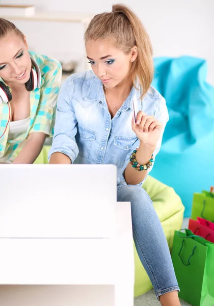 Två unga kvinnliga systrar sitter på soffan i vardagsrummet, hemma, att göra shopping online på digitala tablett, hålla ett kreditkort — Stockfoto