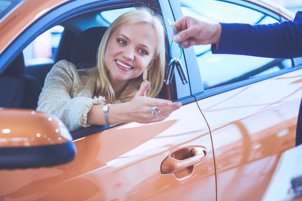 Όμορφη νεαρή γυναίκα παίρνει το κλειδί και χαμογελώντας, ενώ κάθεται σε ένα νέο αυτοκίνητο στην αντιπροσωπεία — Φωτογραφία Αρχείου