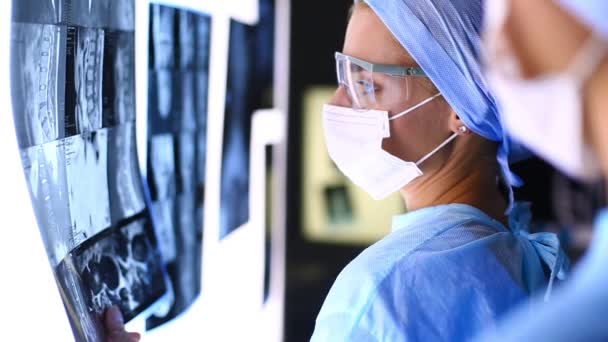 El médico examina los rayos X, sosteniéndolo en las manos en el interior. Los médicos que trabajan juntos en el consultorio, están examinando una radiografía de los pacientes y discutiendo el diagnóstico y el tratamiento — Vídeo de stock