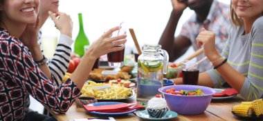Ahşap masada otururken birlikte yemek yiyen bir grup insanın üst düzey görüntüsü. Masada yemek var. İnsanlar fast food yiyor..