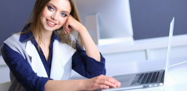 Ofis masasında çalışan ve dizüstü bilgisayarla yazan kendine güvenen genç bir iş kadını.