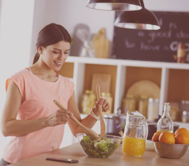 Gülümseyen genç kadın mutfakta taze salata karıştırıyor..