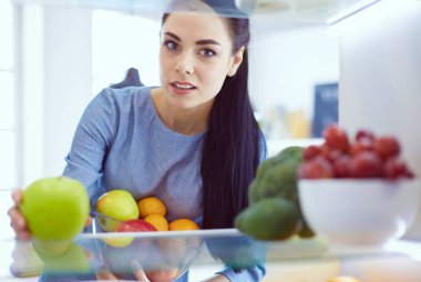 Gülümseyen kadın buzdolabından taze meyve alıyor, sağlıklı yiyecek konsepti.